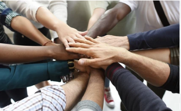 people joining hands in the center of a group circle to signify team work